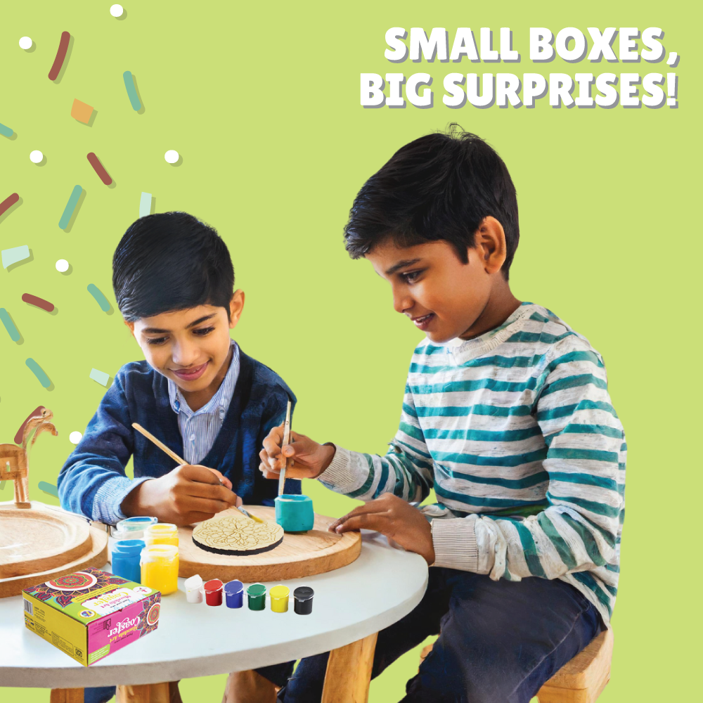 Two children painting Kalakaram's wooden mandala coaster from the minis collection at a table with a green background and text 'Small Boxes, Big Surprises!'.