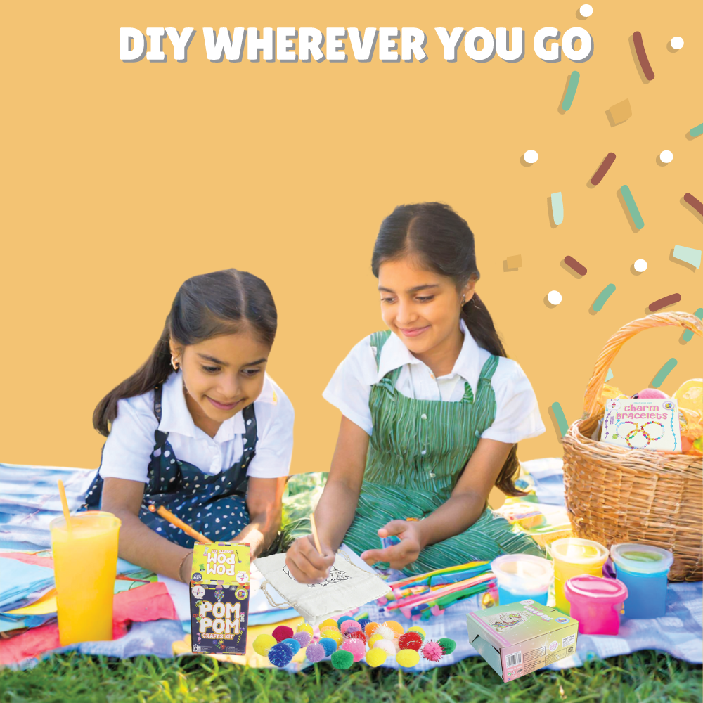 Two young girls sitting on a blanket outdoors with kalakaram's art supplies and a basket with kalakaram's charm bracelet kit, against a yellow background with text 'DIY WHEREVER YOU GO'.